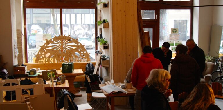 Ein Café mit vielen hellen Holzelementen in dem mehrere Menschen an verschiedenen Tischen sitzen und stehen
