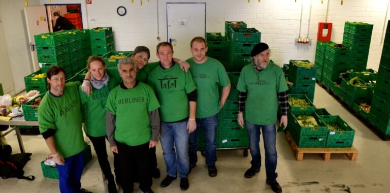 Sieben Personen in grünen T-Shirts bei der Berliner Tafel mit grünen Kisten voller Lebensmitteln hinter ihnen