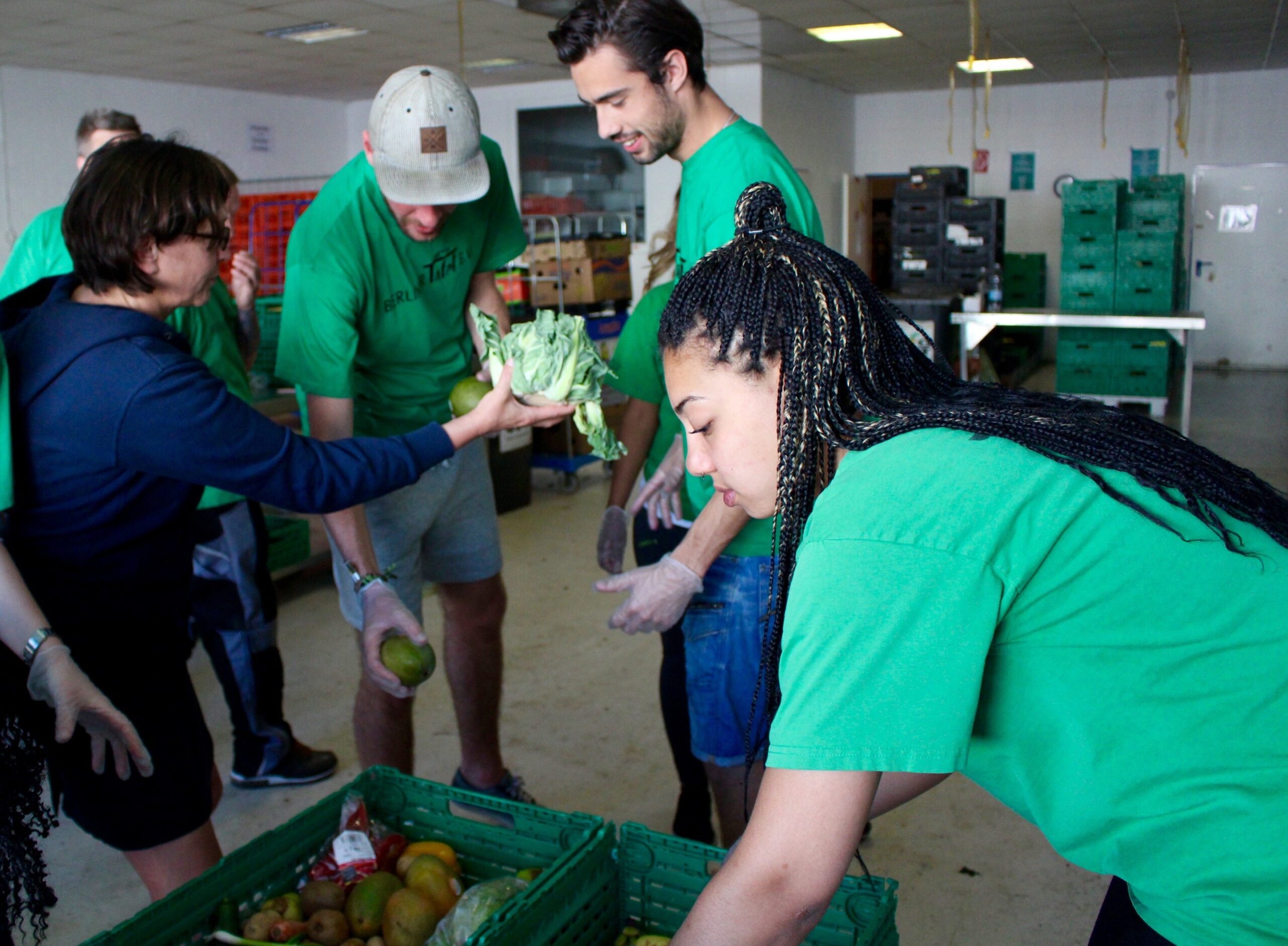 Mehrere Menschen in grünen T-Shirts beugen sich über Kisten mit Lebensmitteln und Verteilen diese