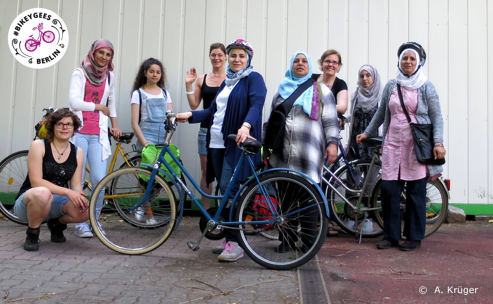 Mehrere Frauen stehen beisammen, einige mit Fahrrädern und Helmen, oben links im Bild das Logo der Organisation Bikeygees