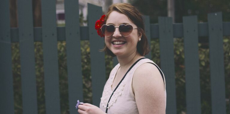 lachendes Mädchen mit Sonnenbrille und Blume im Haar