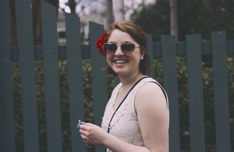 lachendes Mädchen mit Sonnenbrille und Blume im Haar