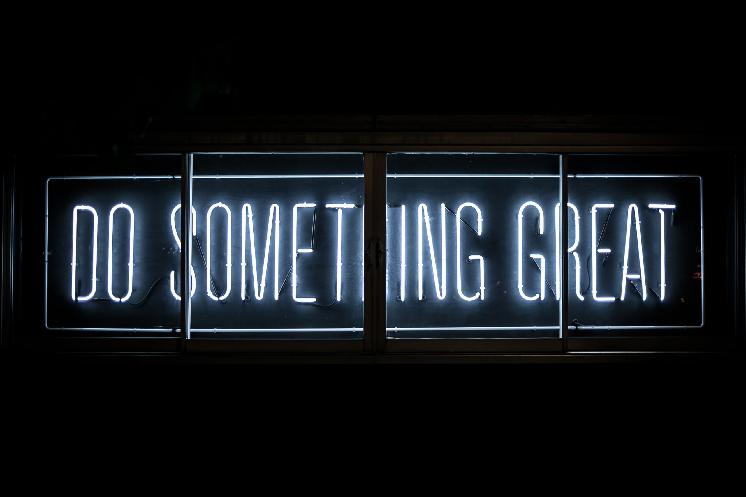 Ein Schild in der Dunkelheit, in blauem Licht steht geschrieben: DO SOMETHING GREAT