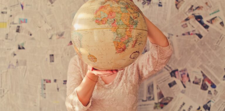 Ein Mädchen hält einen Globus vor ihr Gesicht, im Hintergrund Zeitungspapier.