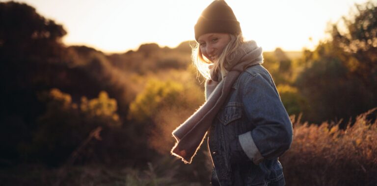 Eine lachende Frau mit Schal und Mütze in der Natur.