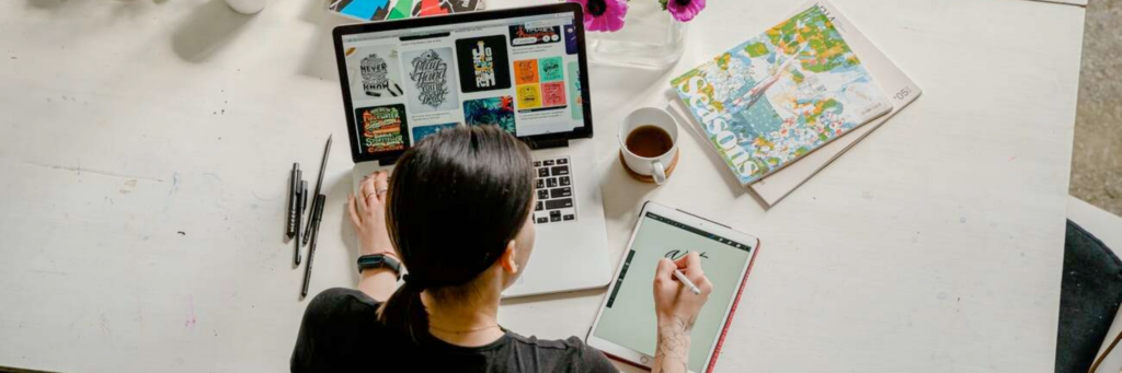 Designerin aus der Draufsicht, wie sie am Laptop und mit Tablet Entwürfe für Designs gestaltet
