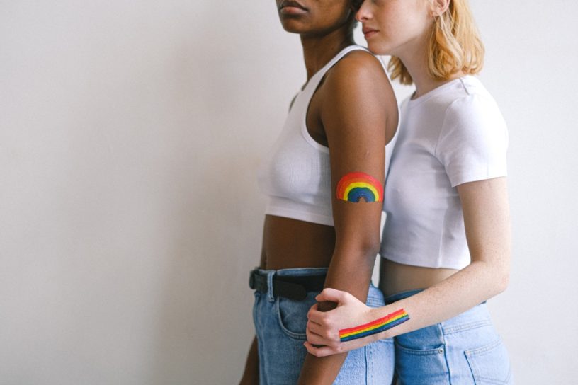 Zwei Frauen stehen nebeinander mit Regebogenfarben auf dem Arm