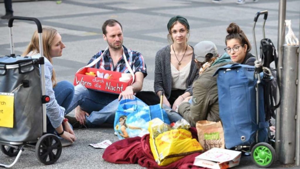 4 junge Menschen unterhalten sich mit einem Obdachlosen Menschen