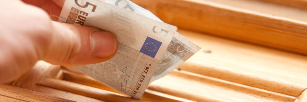 Person steckt einen 5-Euro-Schein in eine Box