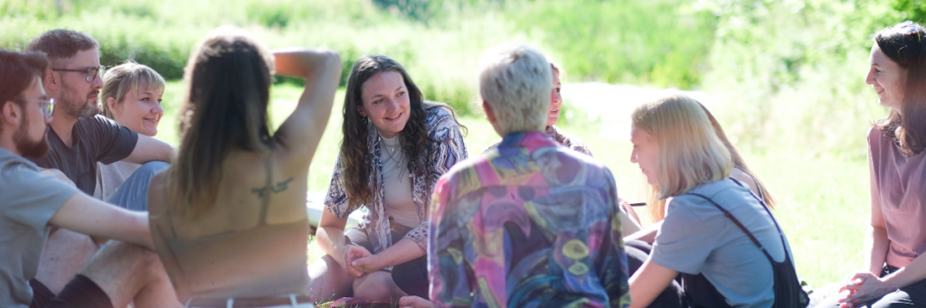 A group of people sitting together on a meadow, looking relaxed. 