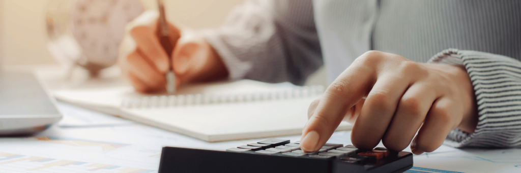 A person typing numbers into a calculator with one hand and writing on a pad with the other.  