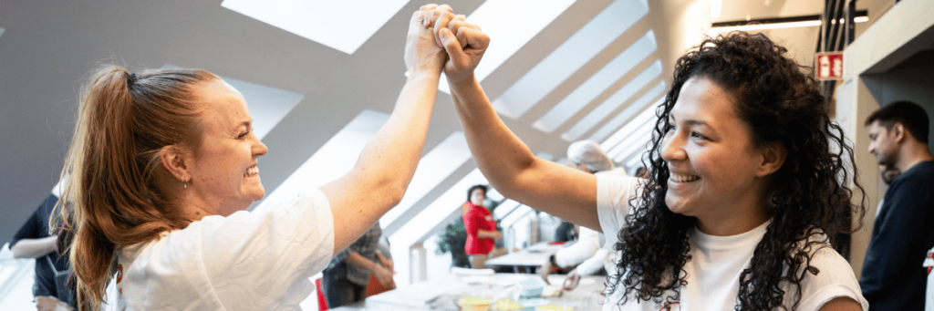 Two women clasp hands and rejoice together.
In the background you can see tables covered with handicrafts.   