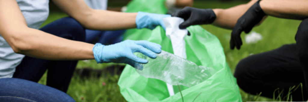 The hands of two people packing garbage from a meadow into a bin bag.