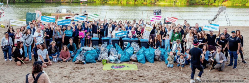 A group photo with lots of people on the beach. In front of them are filled garbage bags. 