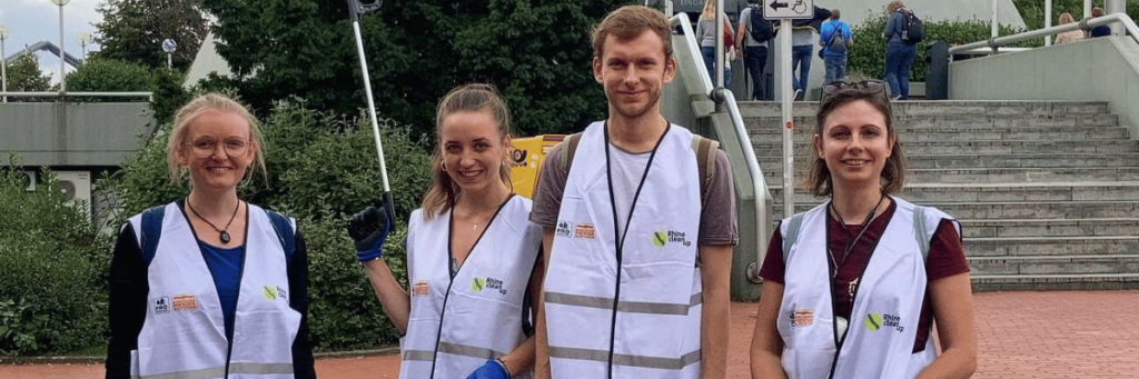 Vier junge Menschen in weißen Warnwesten und mit Müllgreifern in der Hand.