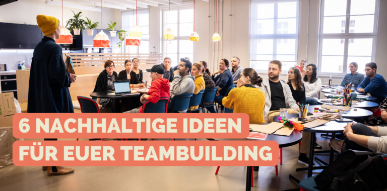 Eine Gruppe von Mitarbeiter*innen sitzt am Tisch und hört einer Person bei einer Anleitung zu.