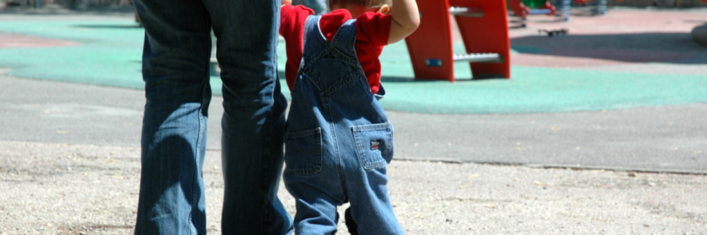 Intermediate picture: Volunteering with family - An adult holds the arms of a child while they are on a playground