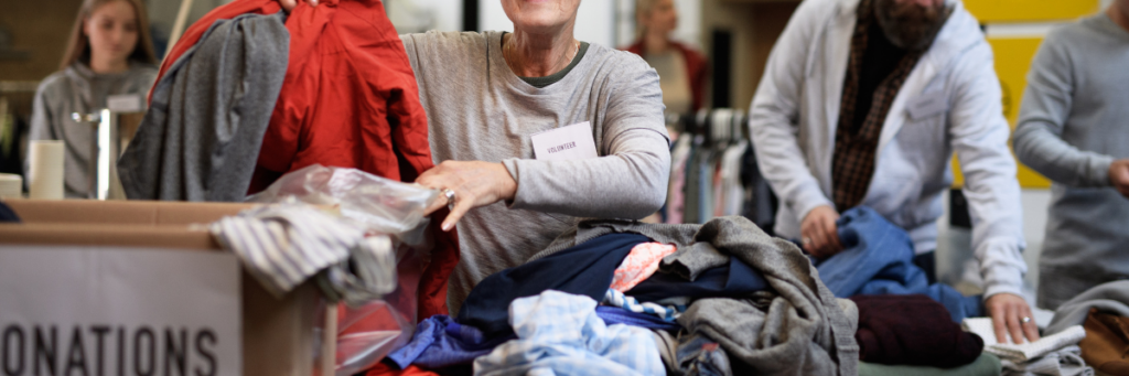 Zwischenbild: Ehrenamt mit obdachlosen Menschen - Menschen sortieren gespendete Kleidung.